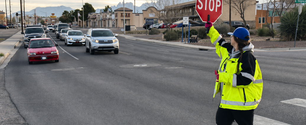A school crossing guard holds a stop sign as vehicles wait near a Las Cruces crosswalk.