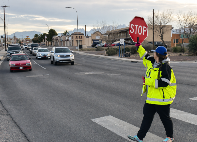 A school crossing guard holds a stop sign as vehicles wait near a Las Cruces crosswalk.