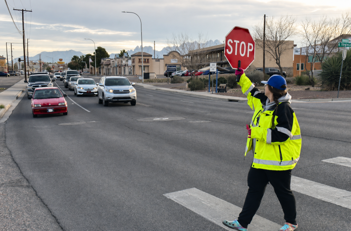 A school crossing guard holds a stop sign as vehicles wait near a Las Cruces crosswalk.