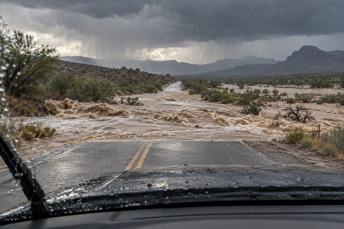 Illustration of heavy rain and floodwater rushing across a roadway, viewed from inside a stopped car.